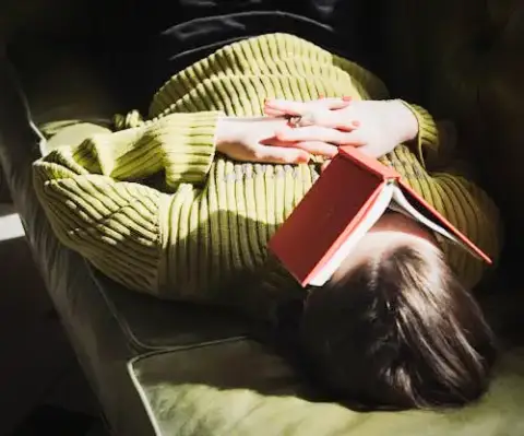 A girl taking a nap with a book over her face.