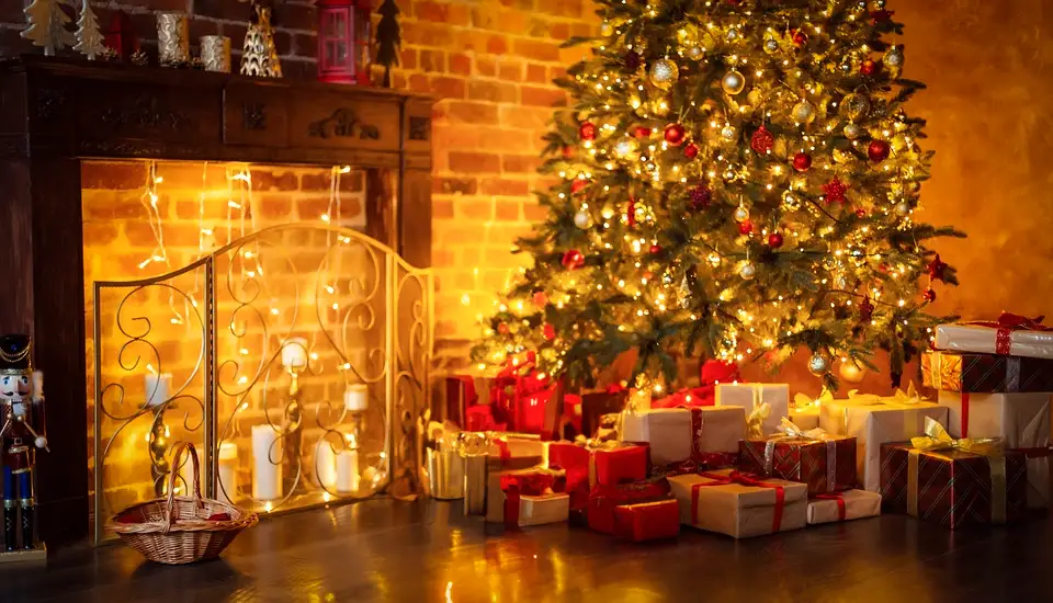 A Christmas tree and presents near a fire place.