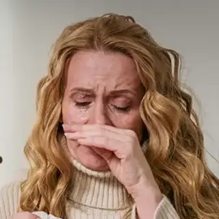 A woman with a tissue, holding her nose, fighting a sneeze.